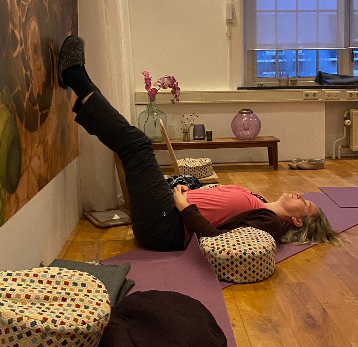 Ik lig met m'n benen omhoog tegen een muur, m'n handen op m'n buik. M'n gezicht wat vertrokken van ongemak, De ruimte is voorzien van meditatiekussens en kaarsjes.